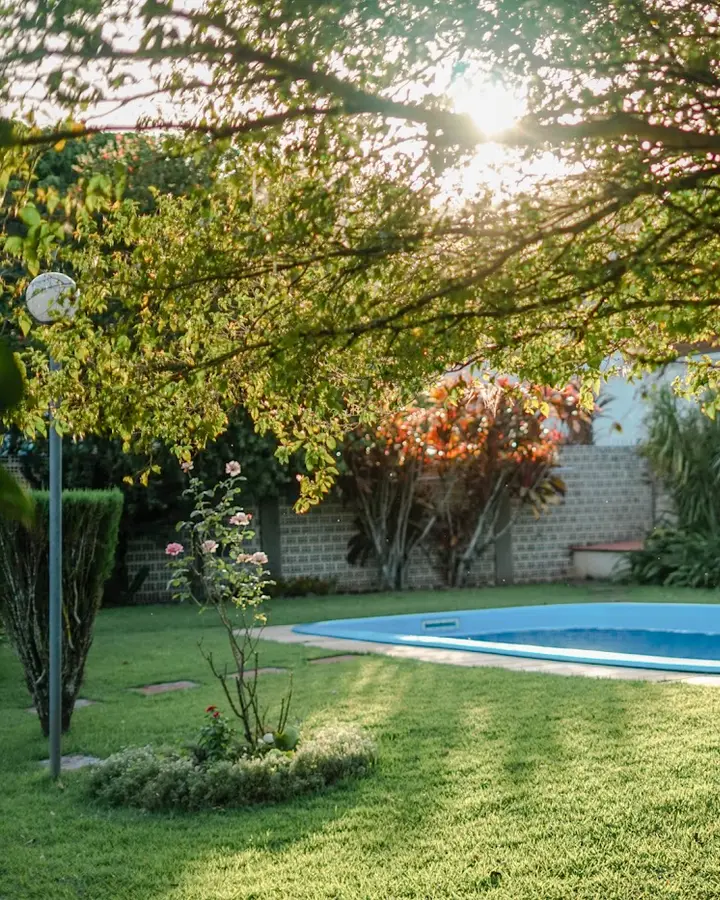Pátio da casa com a piscina sob as árvores no fim da tarde